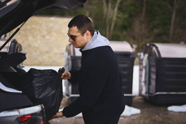 A person loading a bag of waste into a car boot beside communal bins — the kind of trip recurring service saves.